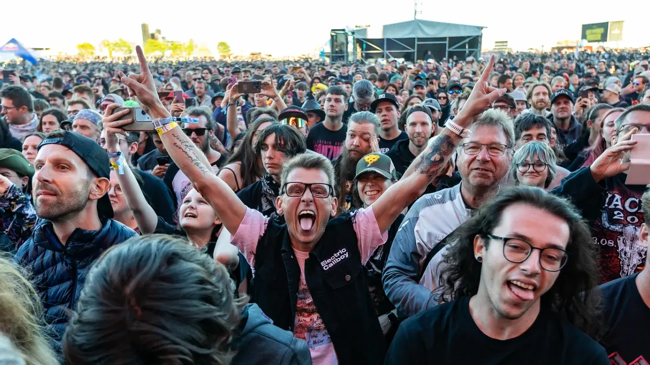 Menge bei einem Musikfestival, jubelt und hebt die Hände, mit einer Person vorne, die eine Electric Callboy Weste trägt.