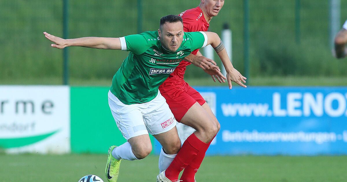 Zwei Fußballspieler in Aktion, einer in Grün und der andere in Rot, kämpfen auf einem Feld.