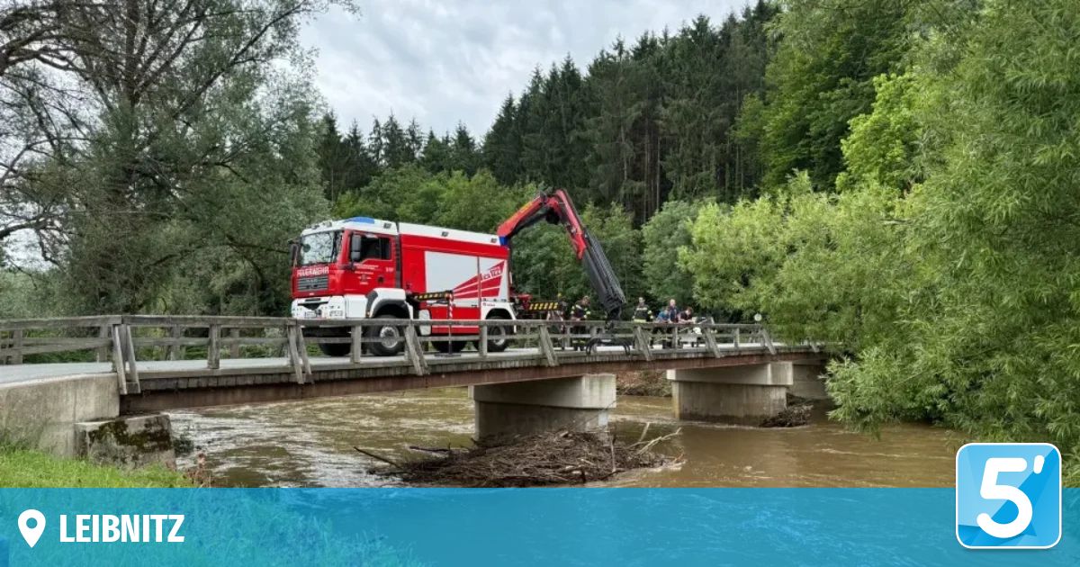 A red and white fire truck with a crane is parked on a bridge over a flowing river. People are standing on the bridge.