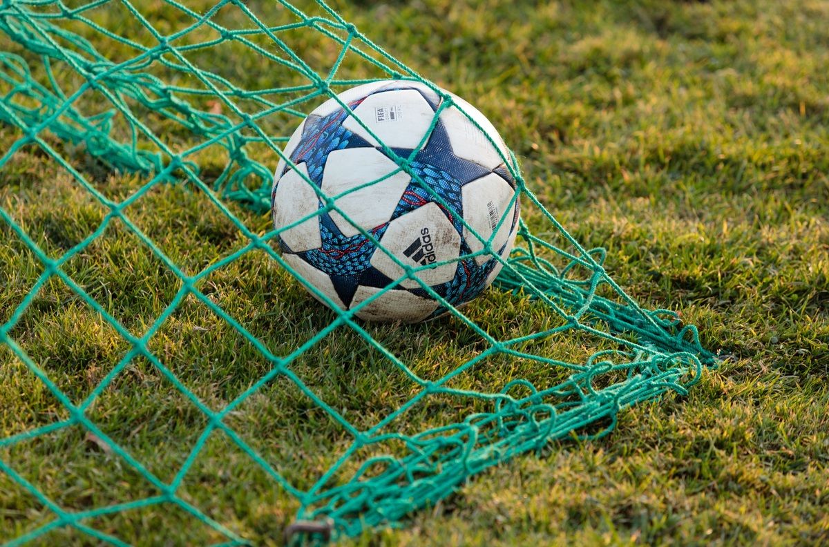A soccer ball is trapped in the net of a soccer goal. The ball has a blue, white, and black pattern. The net is green.