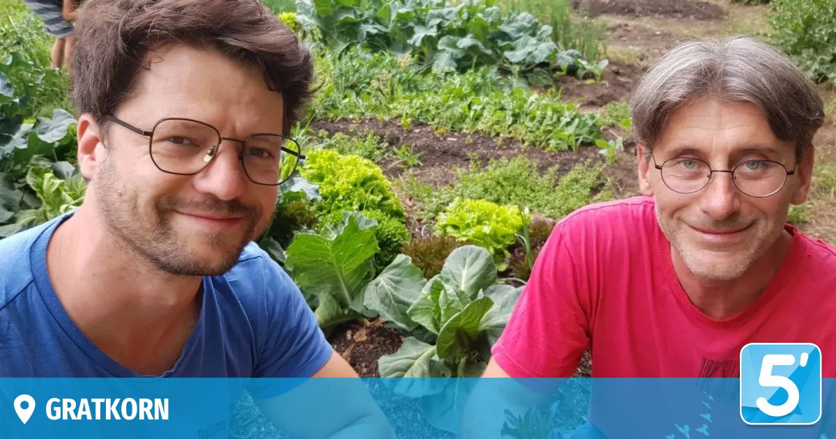 Zwei Männer sind in einem Garten und lächeln für ein Foto mit verschiedenen grünen Pflanzen im Hintergrund.