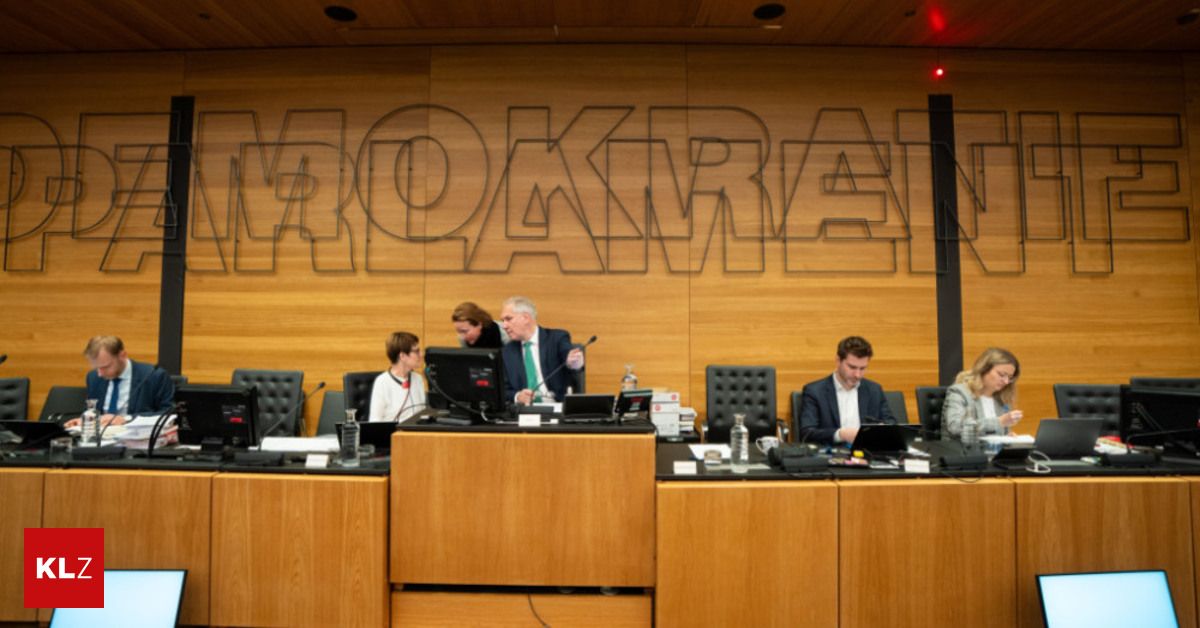 A meeting with several people seated around a table, using laptops. A wall behind them has large letters spelling 'MORKREN'.