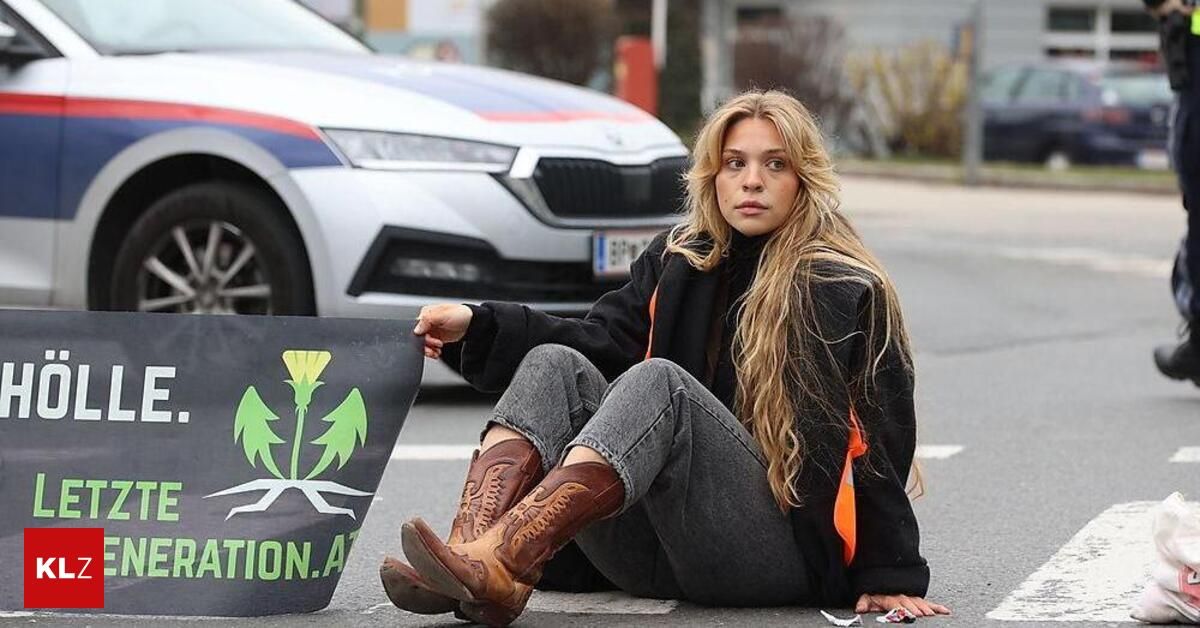 A woman sits on the road with a protest sign, in front of a police car.