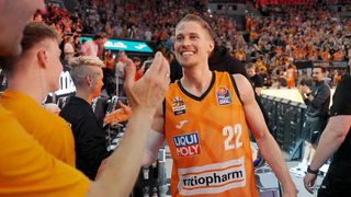 A basketball player in an orange jersey is smiling and celebrating with a fan during a game.