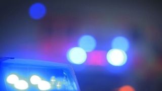 A police car's flashing lights illuminate a blurred background with blue and red lights in the distance.
