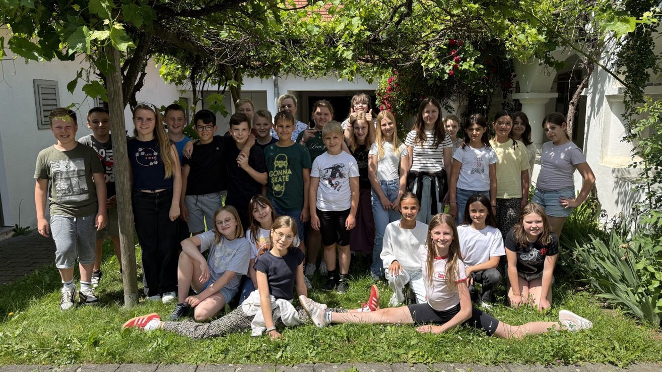 Eine Gruppe von Kindern und Jugendlichen posiert lächelnd für ein Foto vor einem Haus mit viel Grün.