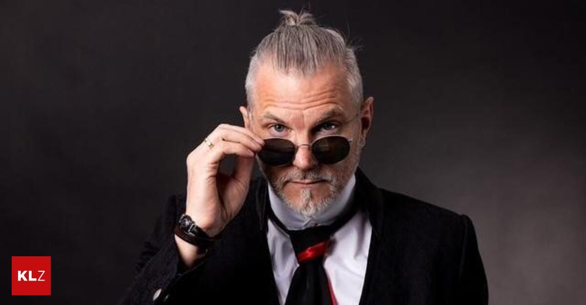 A man in formal attire, holding sunglasses, seems to be posing for a photo.