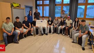 A group of individuals are seated in a room, holding a large check, likely receiving it as a reward or recognition.