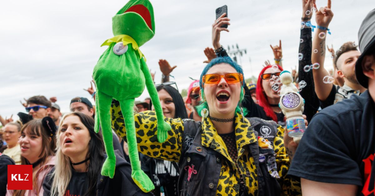 Eine Menschenmenge bei einem Festival, eine Frau hält ein Kermit der Frosch Plüschtier hoch, andere machen Fotos und genießen die Veranstaltung.