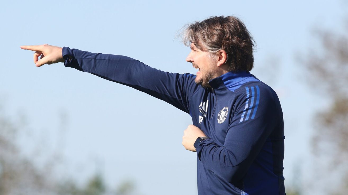 Ein Mann in einem blauen Trainingsanzug mit 'P' auf der linken Brust zeigt mit seiner rechten Hand und lächelt.