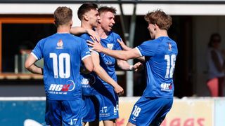 Four soccer players in blue uniforms celebrate on the field. Numbers 10, 17, 41R, and 18 are visible.