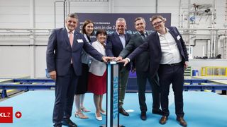 Eine Gruppe von Fachleuten steht um ein Siemens-Schild bei einer Firmenveranstaltung. Sie sind in formeller Kleidung gekleidet und scheinen einen Meilenstein zu feiern.
