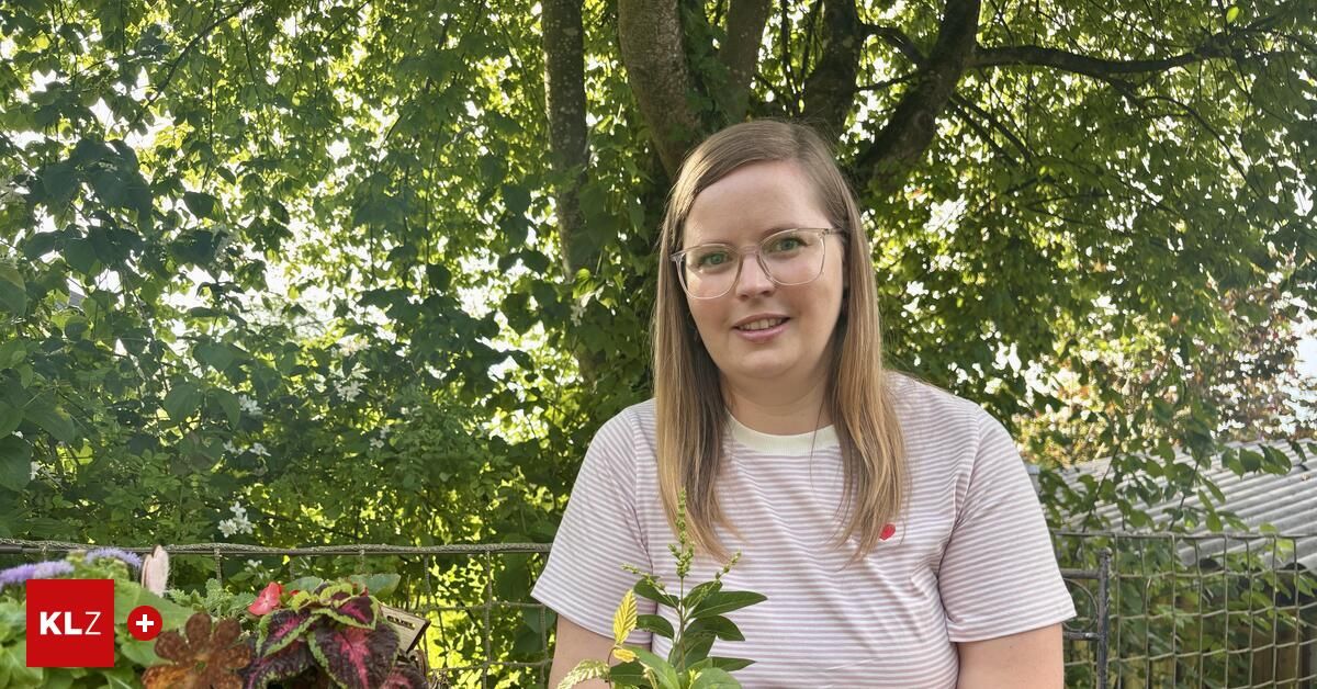 Eine Frau mit Brille und gestreiftem T-Shirt lächelt und posiert in einem Garten mit Pflanzen und Bäumen im Hintergrund.