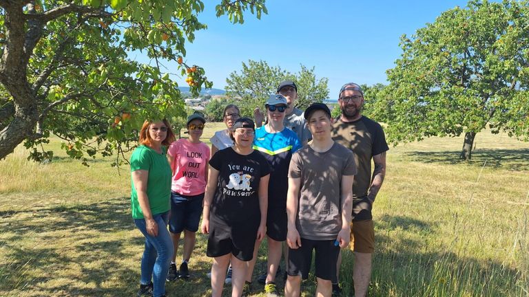 Eine Gruppe von Menschen, Erwachsene und Kinder, steht auf einem Feld unter einem Obstbaum und lächelt für ein Foto.