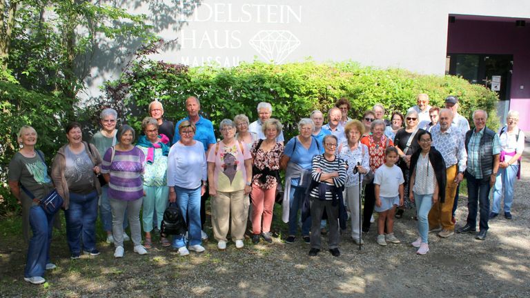 A group of older adults are posing for a photo outside in front of a house called Edelstein Haus.