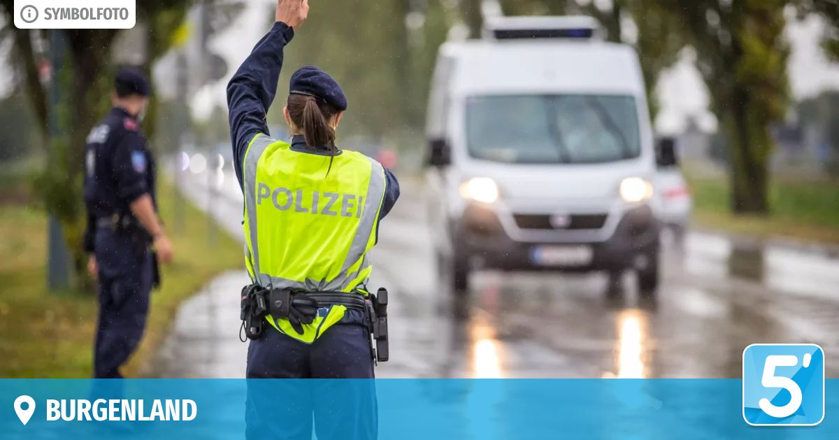 Eine Polizistin in einer reflektierenden Weste signalisiert einem weißen Polizeiwagen an einer verregneten Straße, anzuhalten.