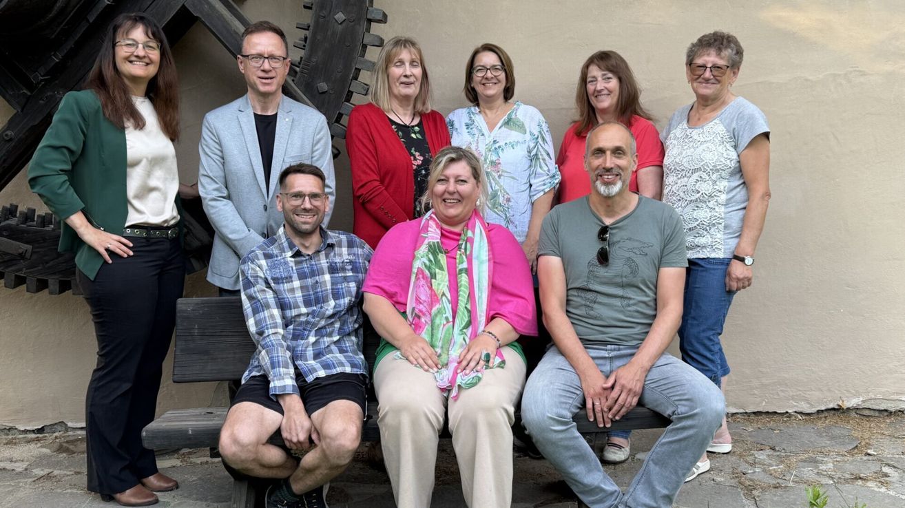 Eine Gruppe von Menschen, darunter Männer und Frauen, lächelt und posiert für ein Foto vor einer Kulisse.