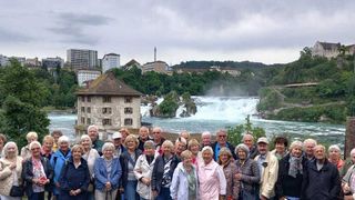 Eine Gruppe von Menschen posiert für ein Foto vor dem Rheinfall in der Schweiz.