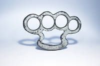 Ein Metall-Knuckle-Duster mit fünf Knöcheln wird auf einer weißen Oberfläche gezeigt. Die Knöchel sind kreisförmig und der Duster sieht alt und abgenutzt aus.