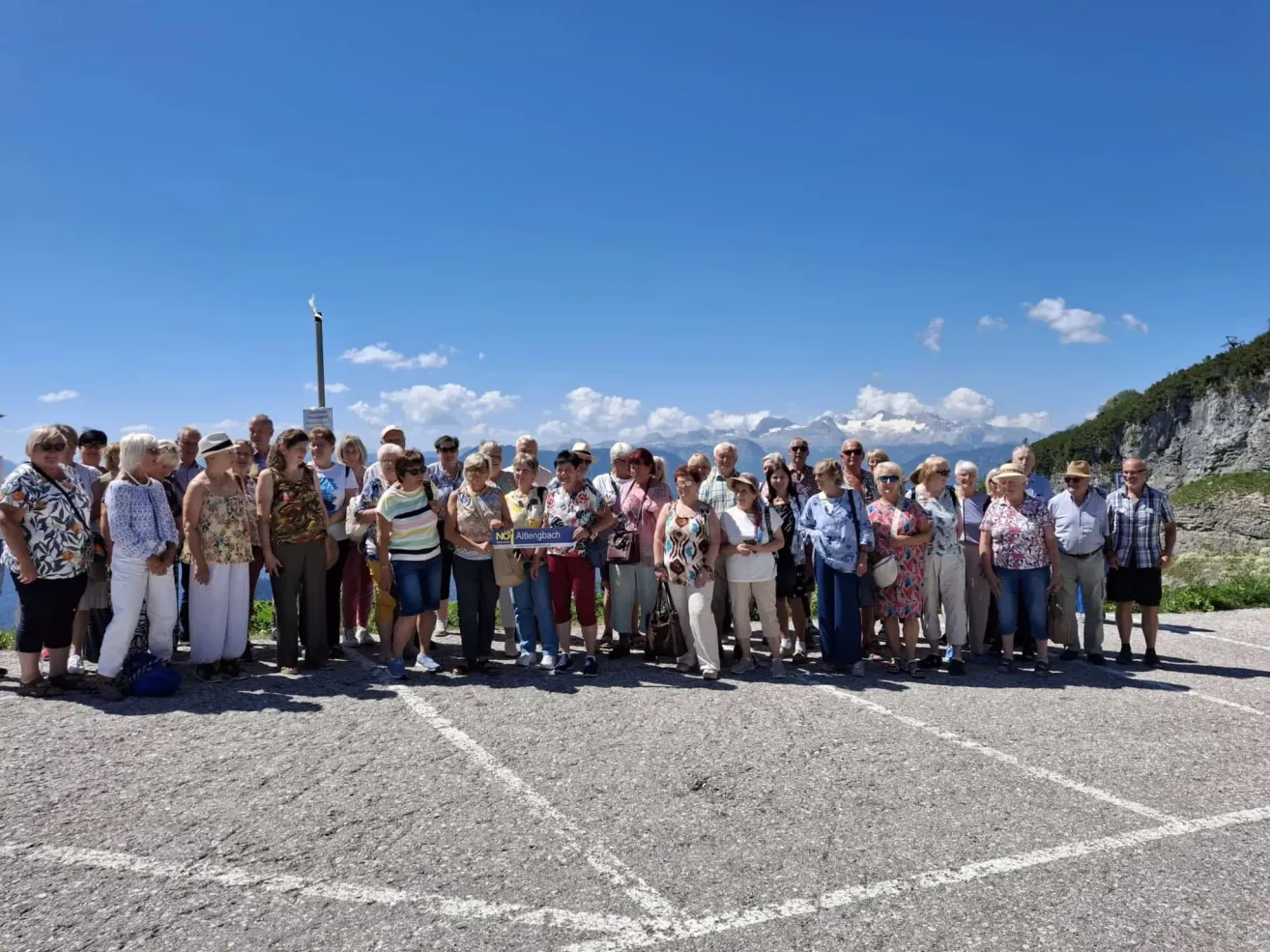 Eine Gruppe von Menschen, die Hüte und Sonnenbrillen tragen, steht zusammen auf einem Parkplatz. Das Wetter ist sonnig.