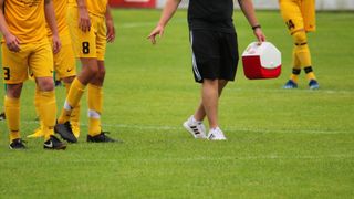 Ein Fußballspieler mit der Nummer 8 läuft auf dem Spielfeld, gefolgt von einem Mann, der einen Kühler trägt.