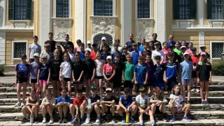 Eine Gruppe von Kindern und Jugendlichen in Sportkleidung posiert für ein Gruppenfoto vor einem klassischen Gebäude mit vielen Fenstern und dekorativen Elementen.