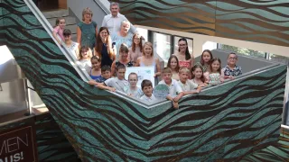 Eine Gruppe von Menschen, einschließlich Kindern, steht vor einer wellenförmigen Struktur und hält ein Zertifikat. Sie lächeln und scheinen zu feiern.