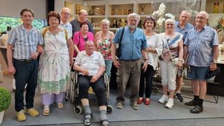 Eine Gruppe älterer Menschen, darunter ein Mann im Rollstuhl, steht gemeinsam in einem Raum mit Regalen voller Vasen.