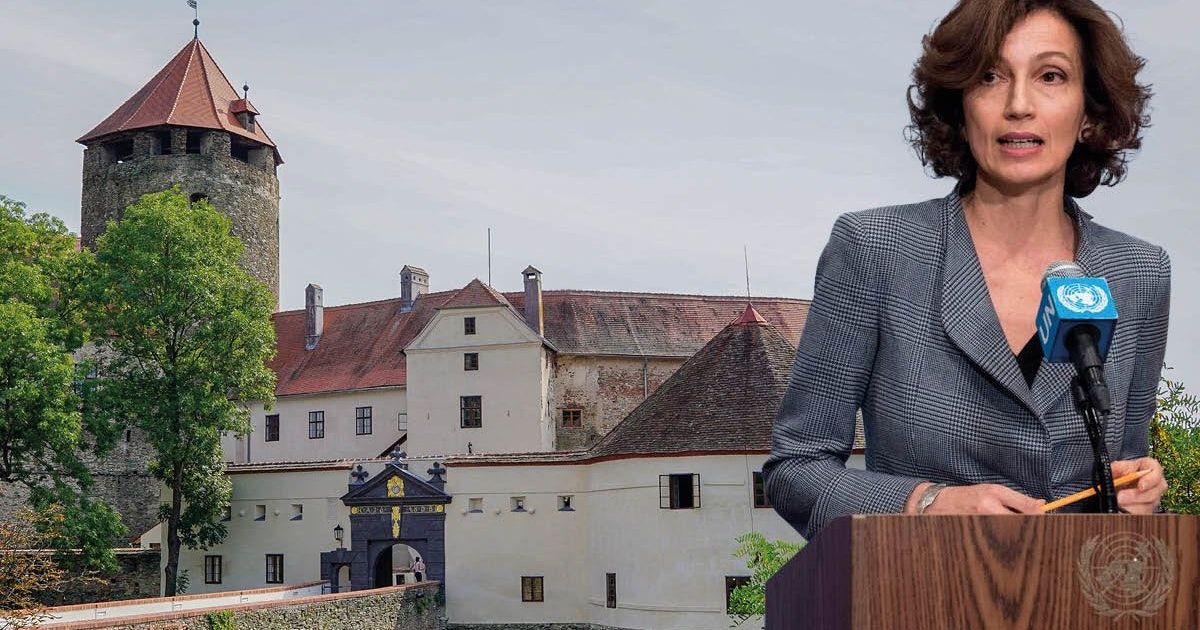 Eine Frau spricht an einem Podium vor einer Burg mit rotem Dach und vielen Fenstern.