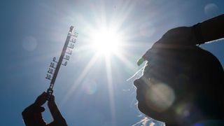 Eine Silhouette einer Person, die ein Thermometer mit der Sonne im Hintergrund hält.