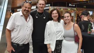 Vier Menschen stehen zusammen in einem Einkaufszentrum und lächeln. Ein Mann in einem weißen Hemd und zwei Frauen, eine in einem weißen Blazer und eine in einem grauen Tanktop.