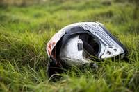 Ein beschädigter Helm liegt auf dem Gras. Der vordere Teil ist zerbrochen, und es gibt rote Flecken. Das Gras ist grün und gut gepflegt.