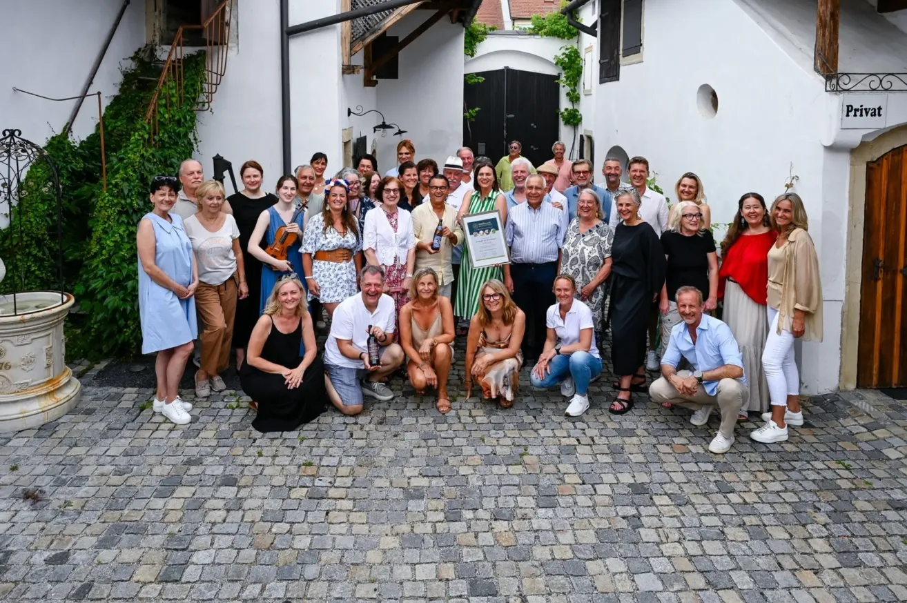 Eine Gruppe von Menschen, wahrscheinlich Kollegen, posiert für ein Foto vor einem Gebäude. Eine Person hält ein gerahmtes Zertifikat.
