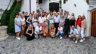 Eine Gruppe von Menschen, wahrscheinlich Kollegen, posiert für ein Foto vor einem Gebäude. Eine Person hält ein gerahmtes Zertifikat.