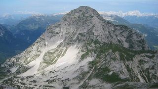 Luftaufnahme eines schneebedeckten Berges mit Flecken von Grün auf seinen Hängen.