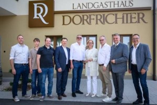 Eine Gruppe von Menschen in Geschäftskleidung steht vor einem Gebäude mit dem Schild Landgasthaus Dorfrichter.