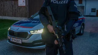 Ein Polizist in Uniform steht mit einem Gewehr vor einem Polizeiauto.