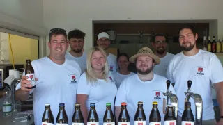 Eine Gruppe von Menschen, gekleidet in weißen Priwi-Markenshirts, steht hinter einem Tisch voller Priwi-Bierflaschen. Sie lächeln und posieren für ein Foto.