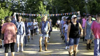 Eine Gruppe älterer Frauen geht gemeinsam auf einer Holzplattform mit Fahnen über ihnen in einem Park.