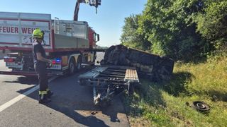 Ein Feuerwehrwagen mit einem Kran hilft am Unfallort, wo ein Fahrzeug auf der Straßenseite umgekippt ist.