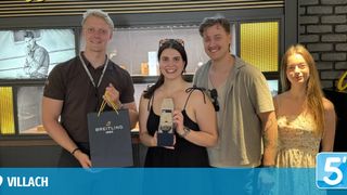 Drei Menschen lächeln in die Kamera, einer hält eine Breitling-Tasche und -Uhr. Sie stehen vor einer Vitrine.