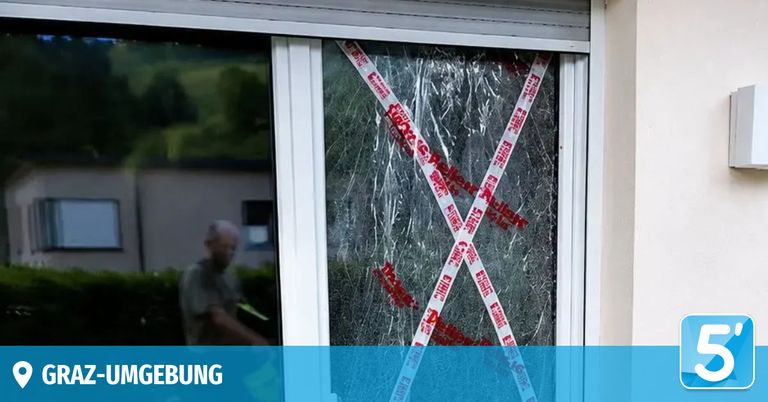 Ein zerbrochenes Fenster mit weißem und rotem Klebeband, auf dem das Wort 'Polizei' steht. Ein Mann geht im Hintergrund vorbei.