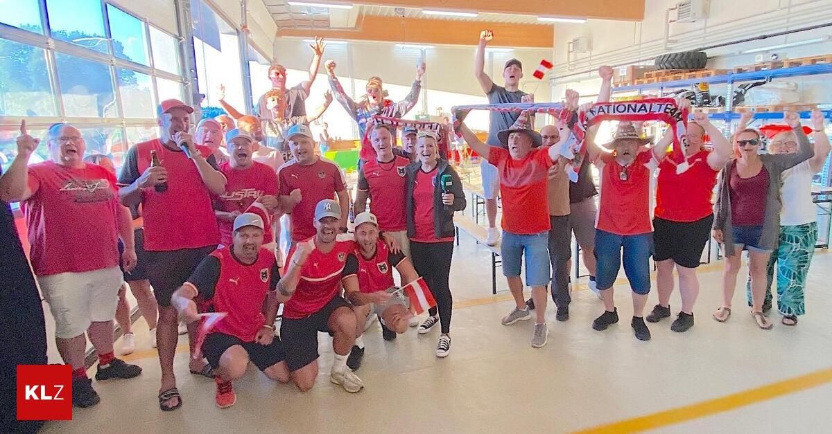 Eine Gruppe von Erwachsenen in Rot posiert für ein Foto in einem Saal, einige knien, während andere stehen und ihre Hände heben.
