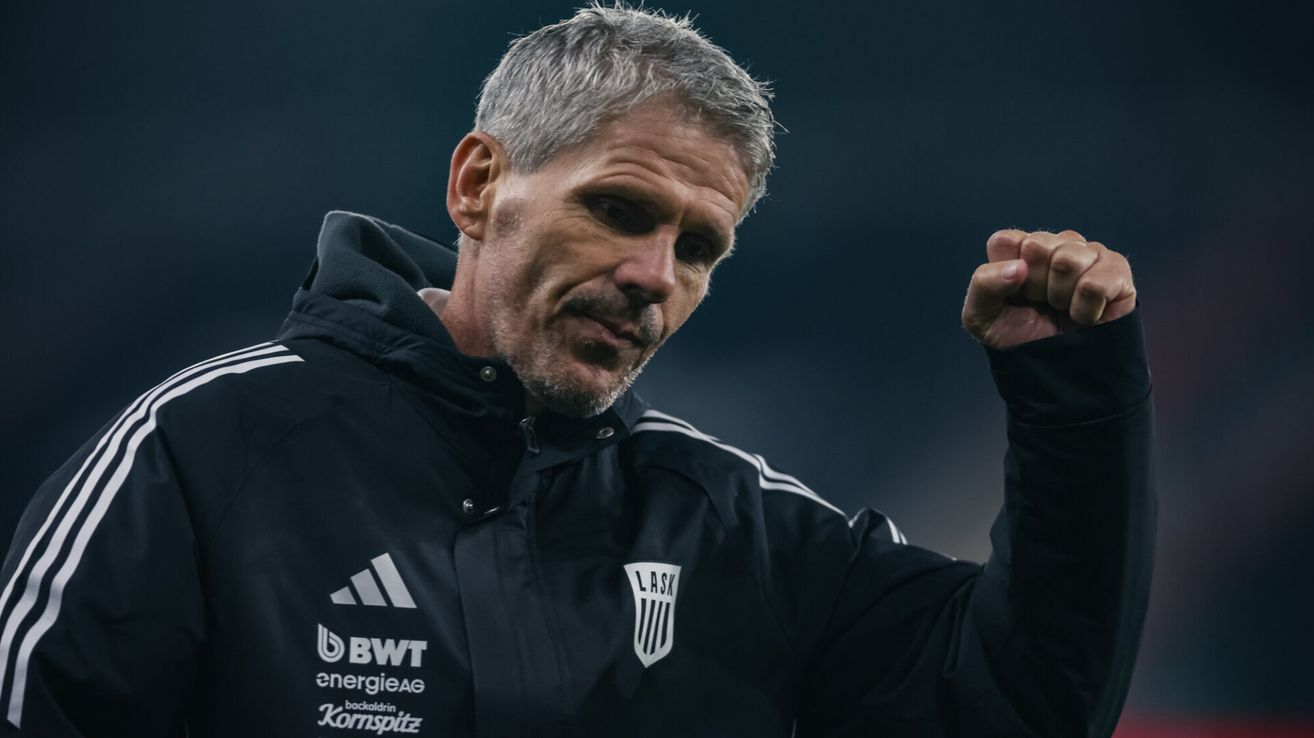 Ein Mann in einem schwarzen Jacke mit weißen Adidas Streifen und den Buchstaben LASK auf der linken Seite. Er sieht nach vorne und scheint zu schreien.