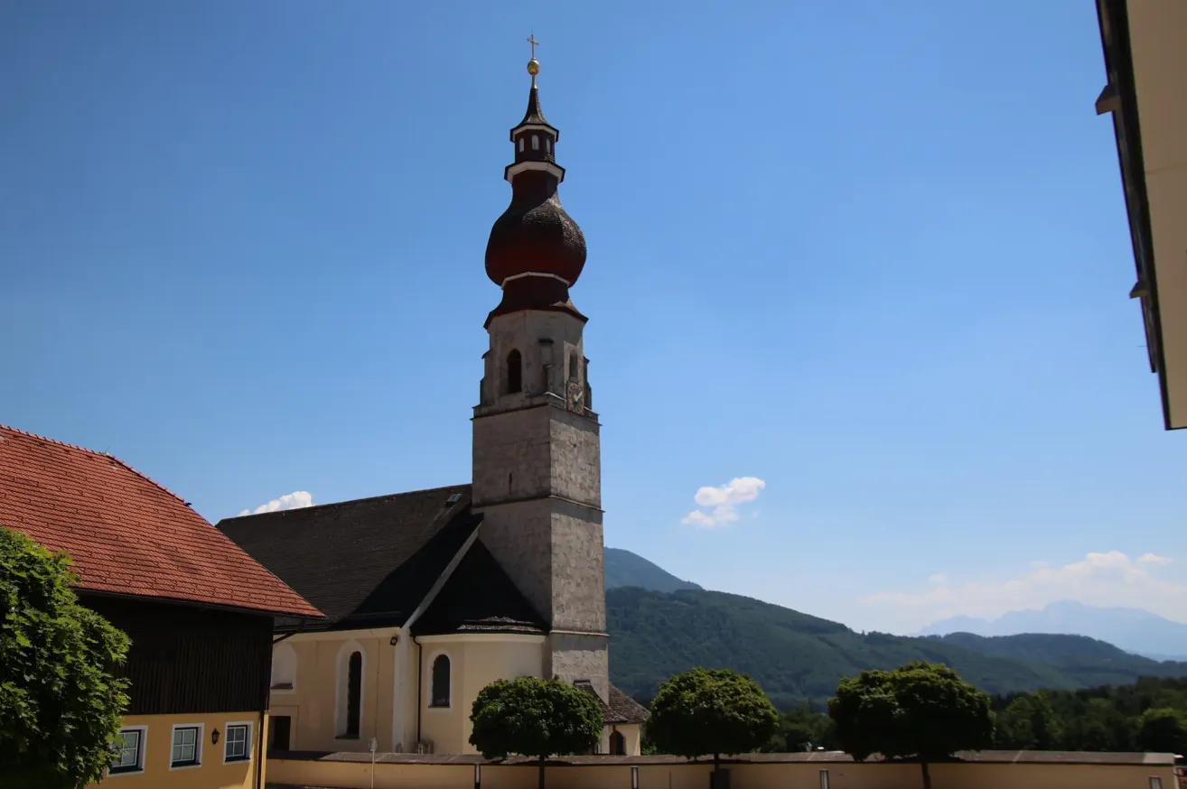 Eine Kirche mit einem hohen Turm und einer Kuppel darauf steht vor einem Berg unter einem klaren Himmel.