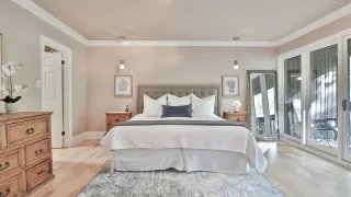 Ein Schlafzimmer mit einem Bett, Holznachtischen und zwei Bilderrahmen an der Wand. Das Bett ist mit weißen und grauen Bettlaken bedeckt.
