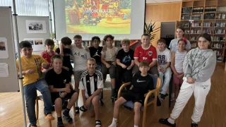 Eine Gruppe von Kindern und Jugendlichen sitzt in Stühlen um eine Beamerleinwand herum, auf der das Spiel Marchenquiz 3 zu sehen ist. Sie lächeln und scheinen Spaß zu haben.
