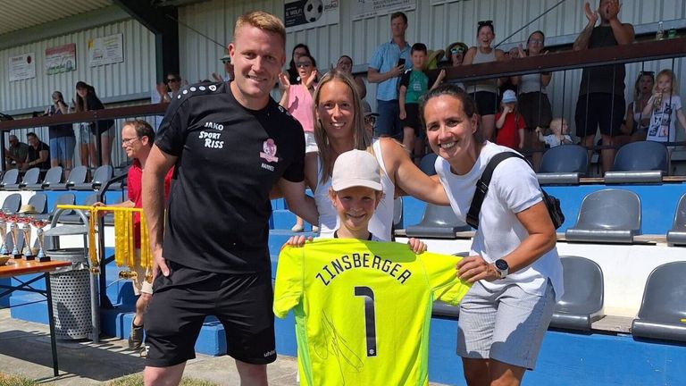 Ein Mann und zwei Frauen posieren mit einem Jungen, der ein signiertes Fußballtrikot mit dem Namen Linsberger hält. Der Mann trägt ein schwarzes Sporttrikot.