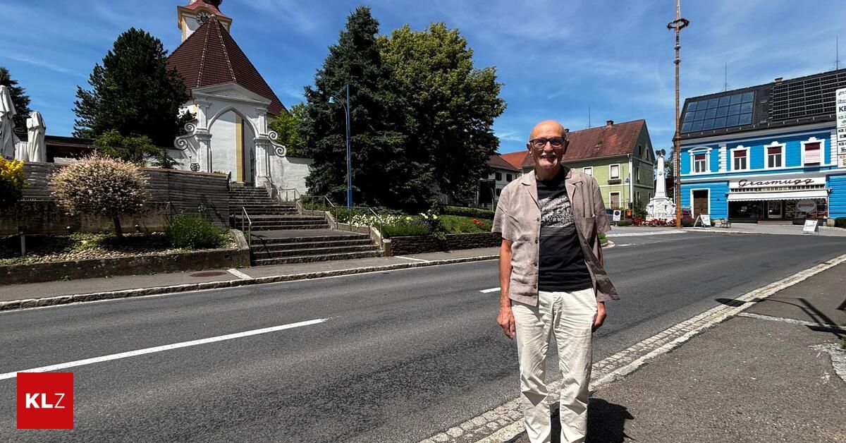 Ein Mann steht am Straßenrand, trägt eine Brille und lächelt, mit einer Kirche und Häusern hinter ihm.