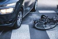 Ein schwarzer Wagen ist auf der Straße geparkt, wobei sich sein Vorderrad auf dem Zebrastreifen befindet. Das Fahrrad liegt auf der Straße.